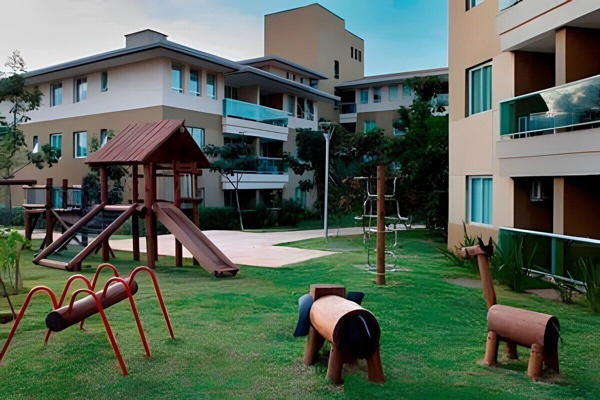 A playground with slides and climbing structures, surrounded by a building with multiple balconies and a flat roof.