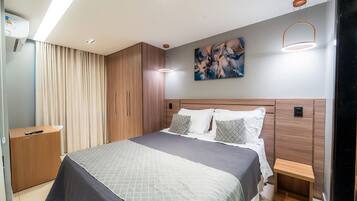 A modern bedroom with a large bed, wooden headboard, a bedside table, a nightstand, a painting on the wall, and a ceiling light fixture.