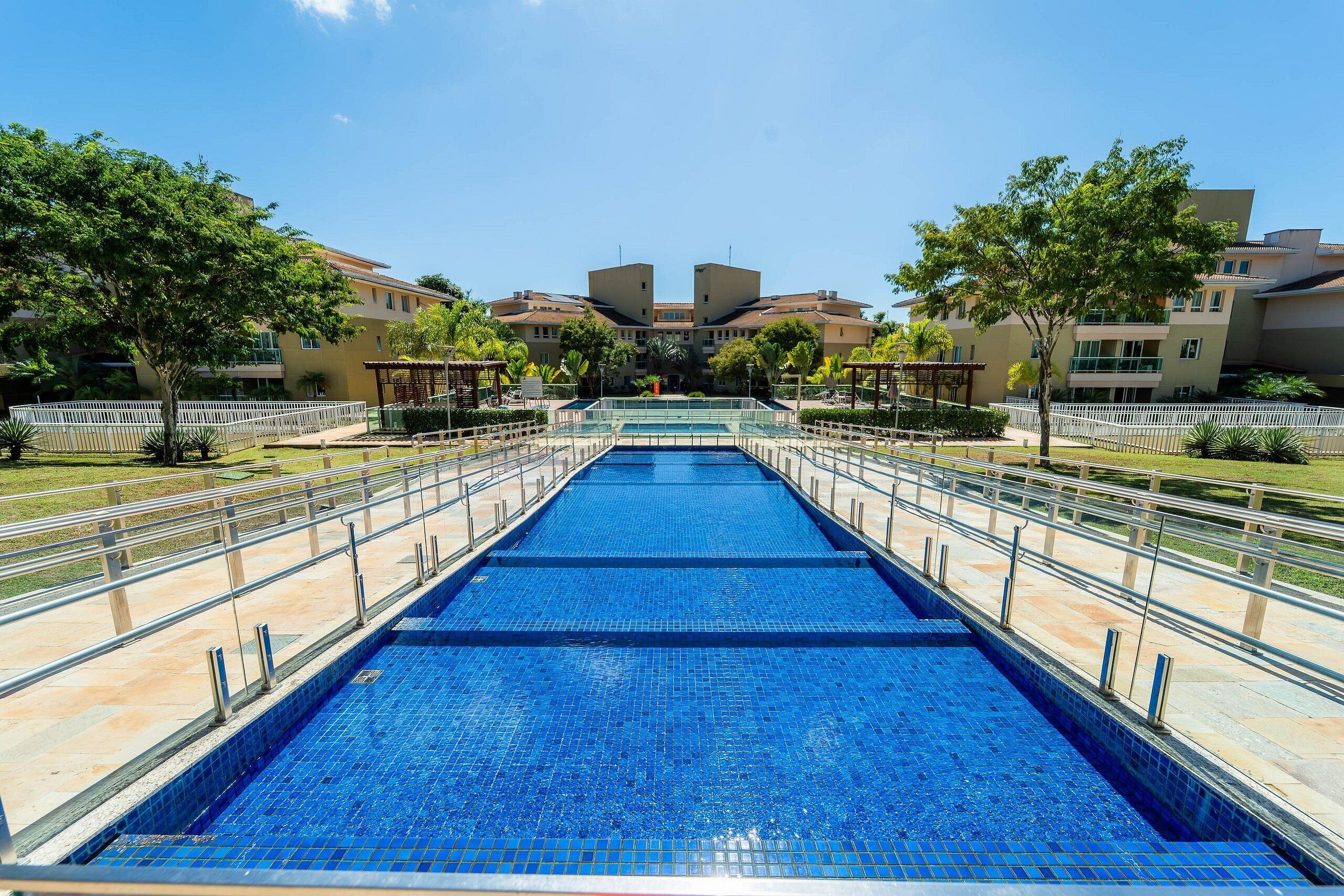 A swimming pool with a tiled deck, surrounded by trees and buildings.