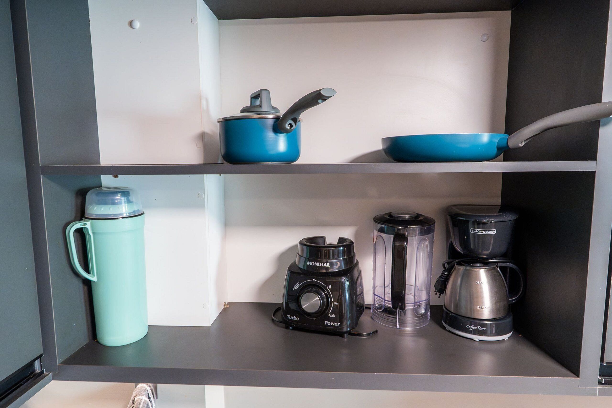 A kitchen with a blue pot, a blue pan, a coffee maker, a blender, and a water bottle on the counter.