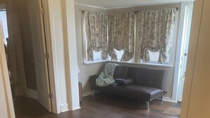 Une pièce avec un grand lit, un canapé de couleur sombre, une fenêtre avec des rideaux et un plancher en bois.
