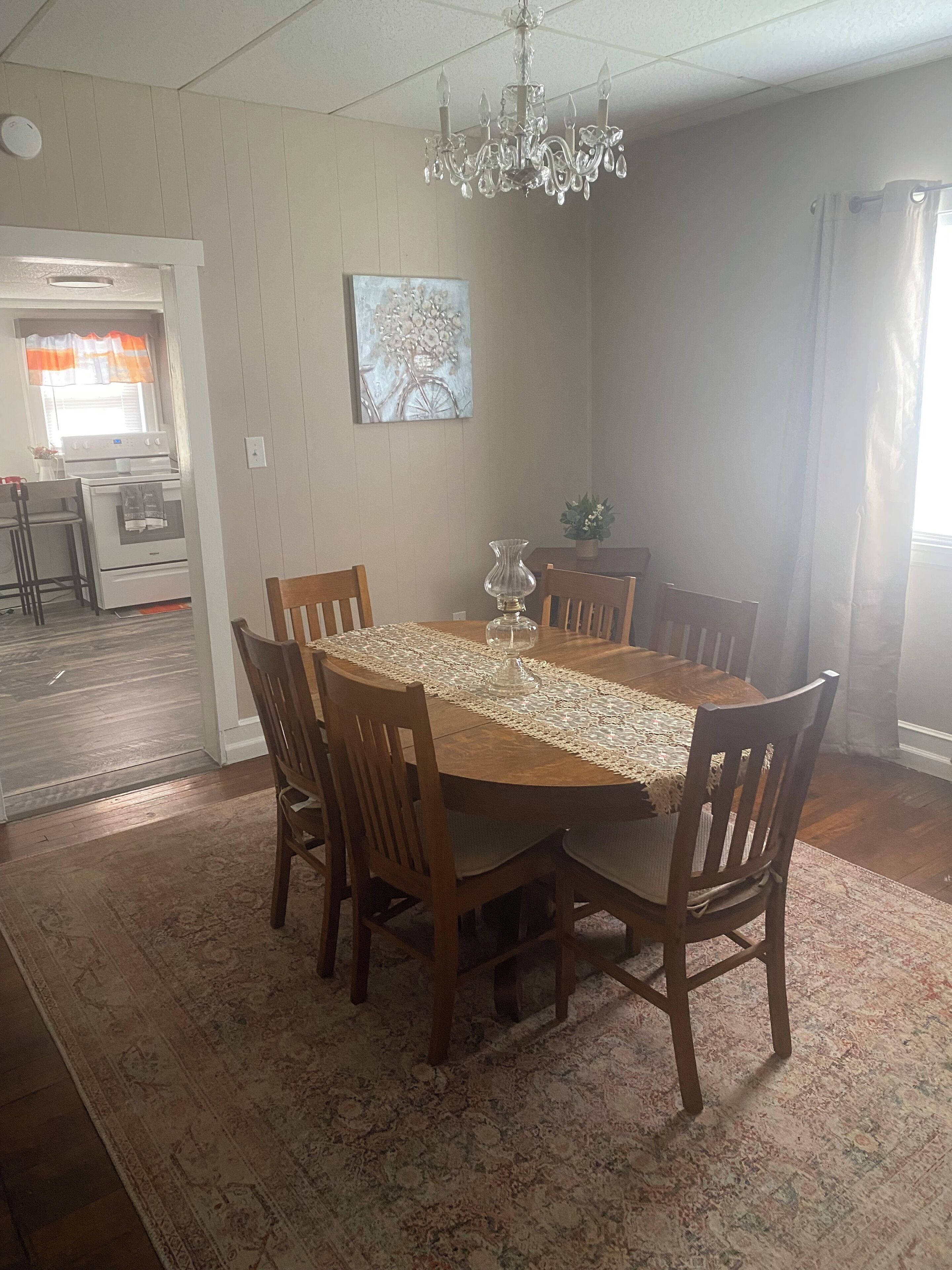 Uma sala de jantar com uma mesa de madeira, cadeiras, um candelabro e um tapete.