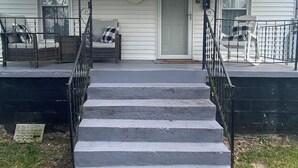 Une maison à deux étages avec un porche, une porte d’entrée et un escalier menant à l’entrée.