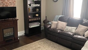 Un salon avec un canapé en cuir, un meuble de rangement en bois foncé, un mur d’accent en briques et un ventilateur de plafond.