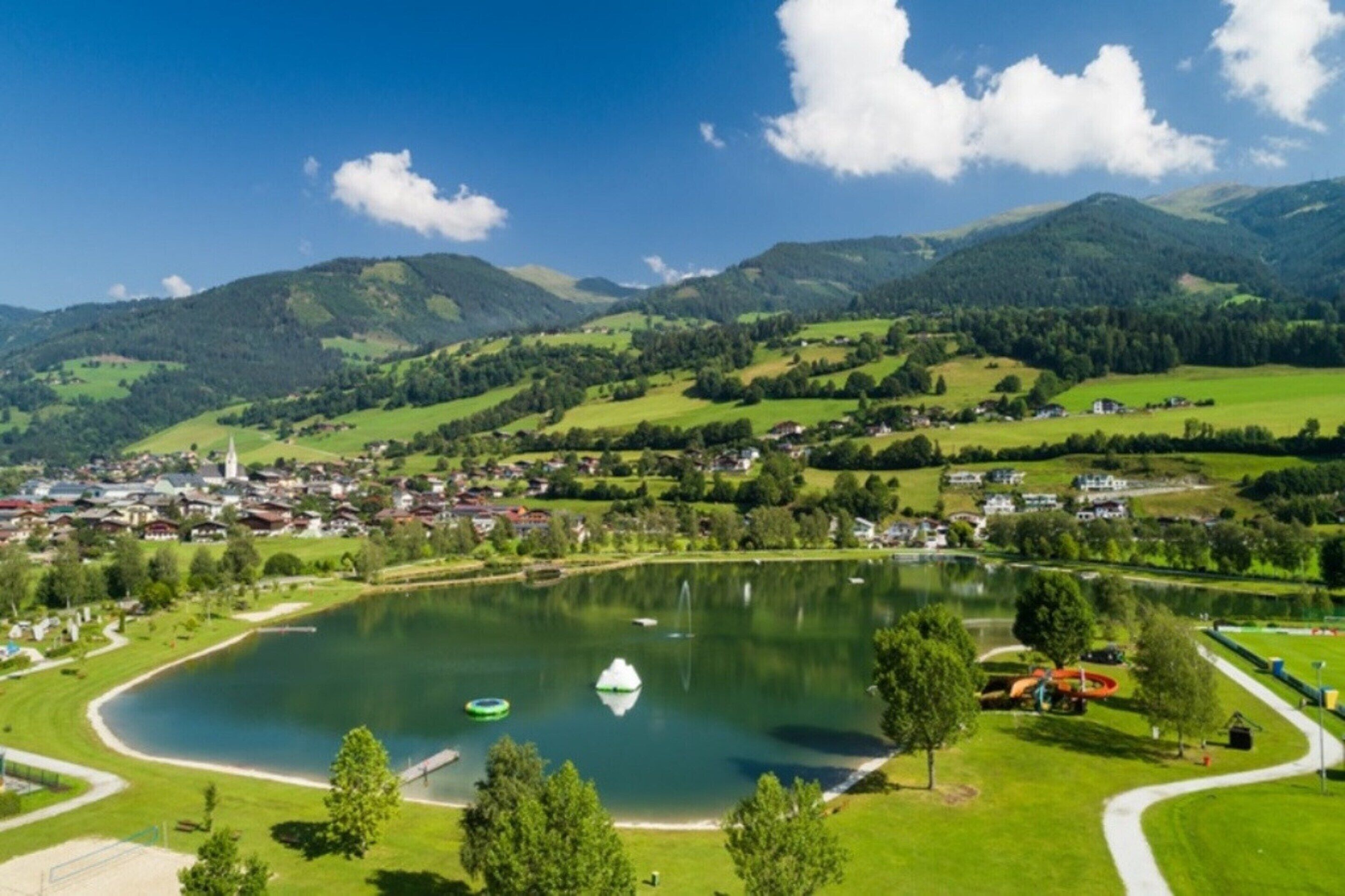 A lakeside view with a small town, green hills, and a clear sky.