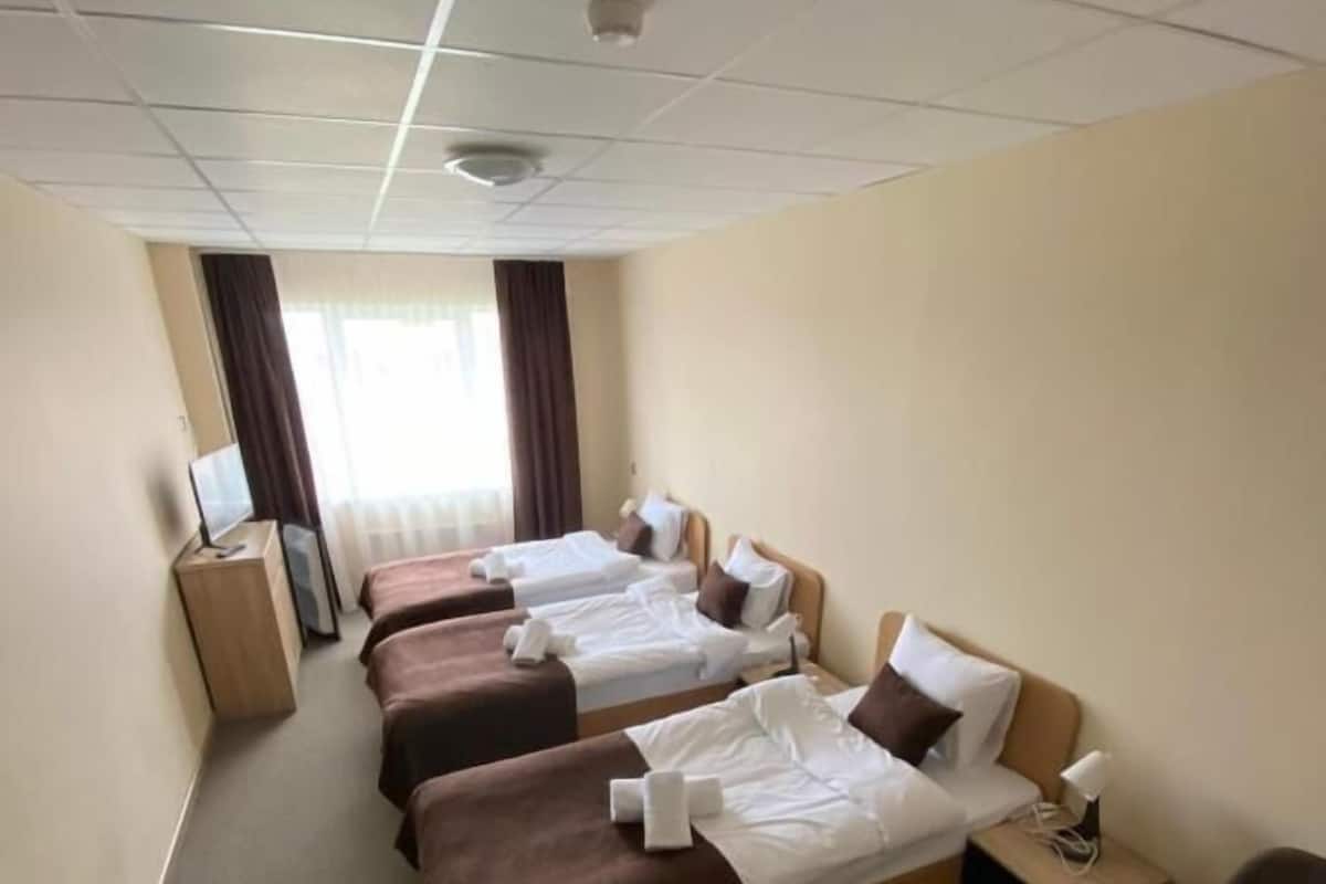 Une chambre d’hôtel avec trois lits, un bureau, une chaise et une fenêtre avec des rideaux.