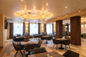 Un hall de hotel espacioso con varias zonas de estar, una lámpara central y grandes ventanales que permiten la entrada de luz natural.