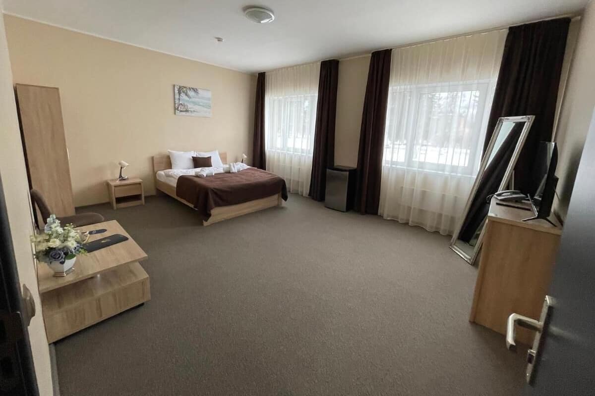 Une chambre d’hôtel avec un lit, un bureau avec une lampe, une télévision et une fenêtre avec des rideaux.