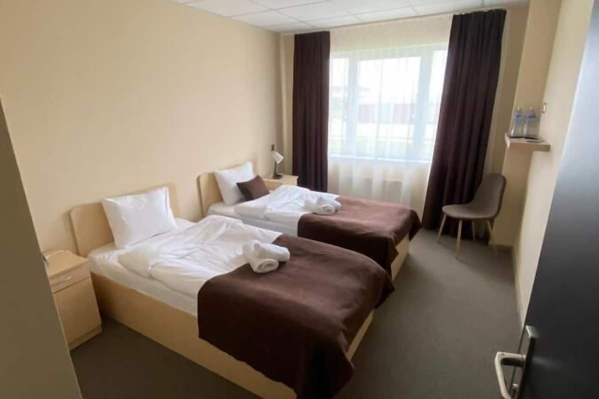 Une chambre d’hôtel avec deux lits, un bureau, une chaise et une fenêtre avec des rideaux.