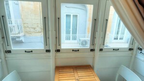En lille balkon med et træbord og to hvide stole, med udsigt over en bygning med balkoner.