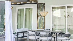 An outdoor dining area with a table and chairs, a hanging light fixture, and a covered seating area with a white canopy.