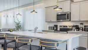 A modern kitchen with a central island, bar stools, stainless steel appliances, and pendant lighting.