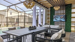 A covered outdoor patio with a pool, seating area, and a large screen displaying a cityscape.