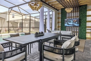 A covered outdoor patio with a pool, seating area, and a large screen displaying a cityscape.