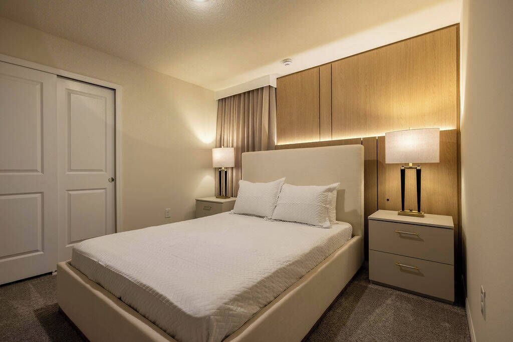 Habitación de hotel con una cama grande, dos mesitas de noche con lámparas, un cabecero de madera y una puerta.