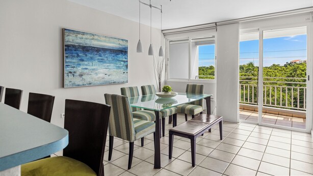 Een eethoek met een glazen tafel en stoelen, een schilderij aan de muur en een balkon met uitzicht.