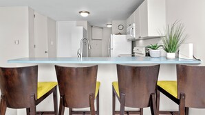 Een moderne keuken met witte kastjes, een blauw aanrecht en een spoelbak. Er staan vier houten stoelen met gele kussens.