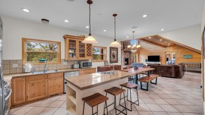 A spacious kitchen with wooden cabinets, a large island with bar stools, and pendant lighting. - Authentic log cabin minutes from Zion NP (Orderville)