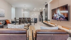 A modern living room with leather sofas, a dining area, and a large TV on the wall.