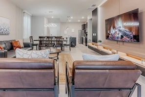 A modern living room with leather sofas, a dining area, and a large TV on the wall.