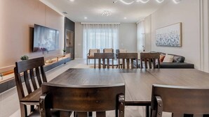 A modern dining area with a wooden table and chairs, a flat-screen TV, and a sofa with cushions.