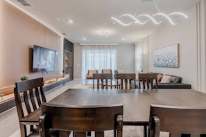 A modern dining area with a wooden table and chairs, a flat-screen TV, and a sofa with cushions.