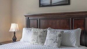 A neatly made bed with a quilted white duvet, two decorative pillows with Parisian prints, a dark wooden headboard, a bedside lamp, and a framed picture on the wall. - 4BR house with pool near Disney area (Kissimmee)