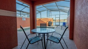 A covered outdoor seating area with a glass table and metal chairs, overlooking a pool and a building with a barbecue grill. - 4BR house with pool near Disney area (Kissimmee)