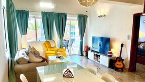 A living room with a sofa, yellow armchair, glass coffee table, and a TV. - On Bavaro Beach - Secure, Gated Condo Community. In Center of Bavaro-Punta Cana (La Altagracia Province)