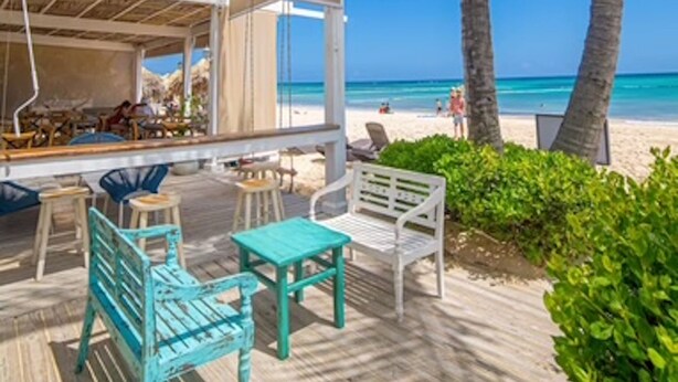 A beachside patio with wooden furniture, a covered seating area, and a view of the ocean. - On Bavaro Beach - Secure, Gated Condo Community. In Center of Bavaro-Punta Cana (La Altagracia Province)