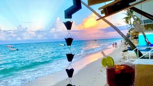 A beach view with a drink on a table, a decorative string of heart-shaped objects, and a boat in the water. - On Bavaro Beach - Secure, Gated Condo Community. In Center of Bavaro-Punta Cana (La Altagracia Province)