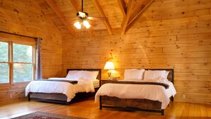 A wooden cabin bedroom with two beds, a ceiling fan, and a large window. - A Slice of Salisbury, Pool,Hot Tub, 10 acres (Salisbury)