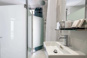 A modern bathroom with a glass shower enclosure, a white sink with a silver faucet, and a shelf with toiletries.