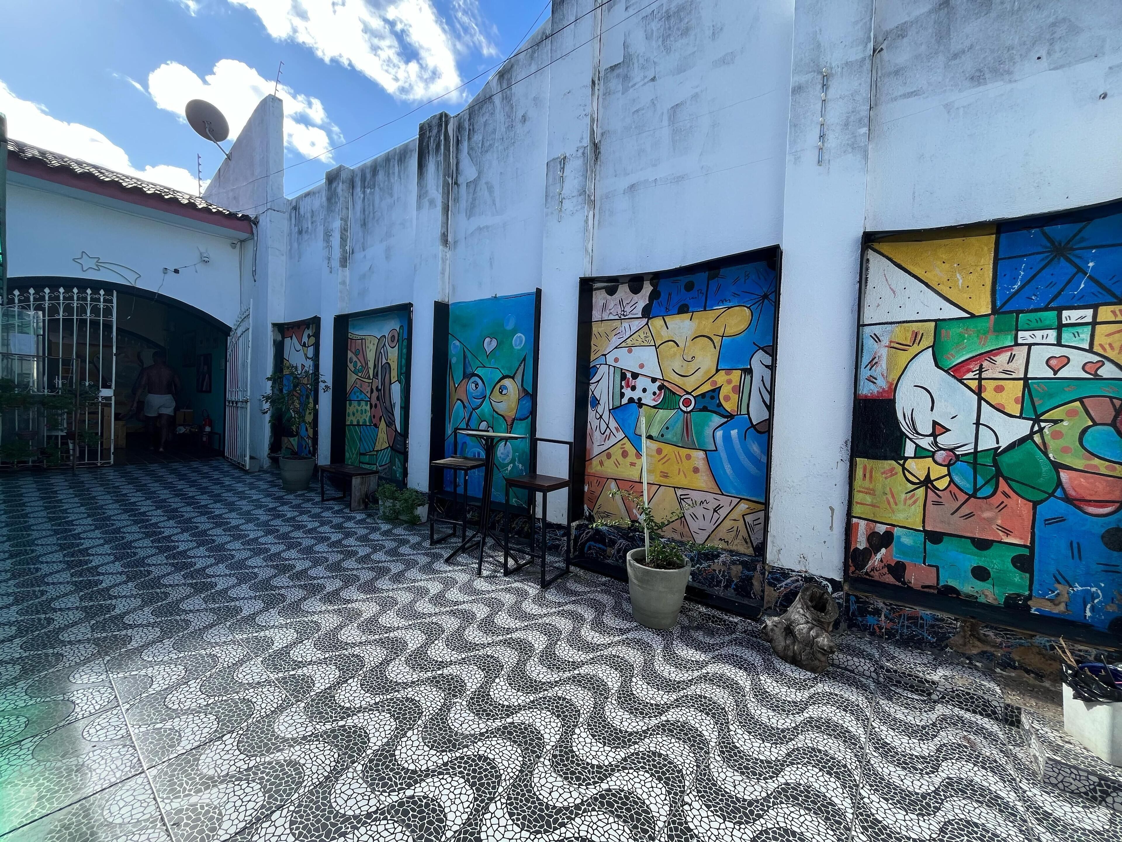 A courtyard with tiled flooring, a gate, and colorful murals on the walls.