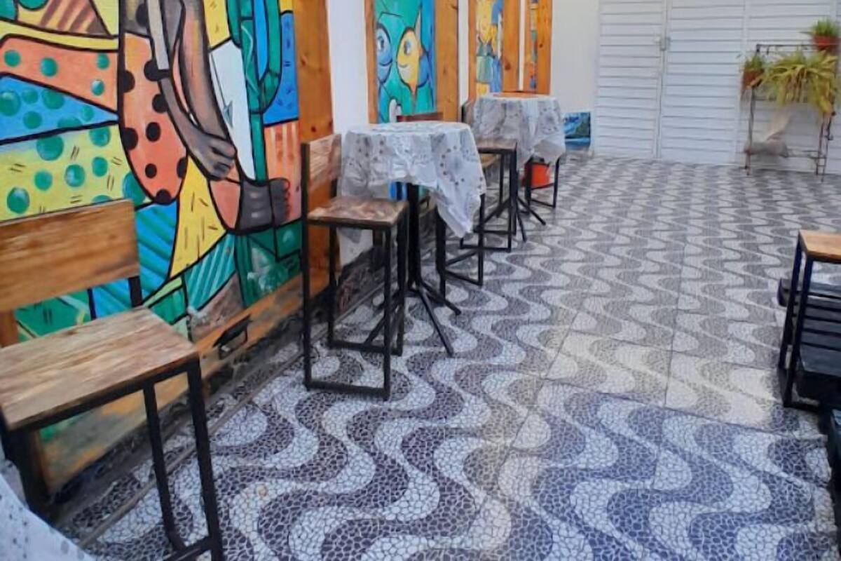 An outdoor patio area with tables and chairs, a tiled floor, and colorful murals on the walls.