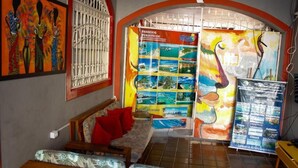 Un hall d’hôtel avec un canapé, un panneau d’affichage orné d’affiches de voyage et une fenêtre avec des barreaux en métal.