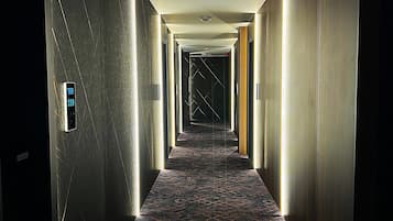 A hotel hallway with a patterned carpet, a digital display, and a fire alarm.