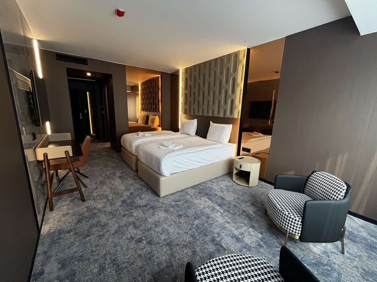 A modern hotel room with a large bed, a desk, a chair, and a TV.