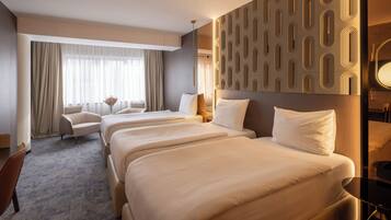 Une chambre d’hôtel avec trois lits, un canapé, un bureau et une grande fenêtre avec des rideaux.