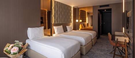 A hotel room with two beds, a desk, a chair, and a vase with flowers.