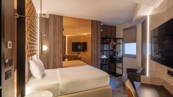 Una habitación de hotel moderna con una cama grande, televisión, zona de estar y armario.