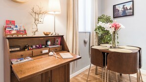 A wooden desk with a lamp, a vase with flowers, and a framed picture on the wall.