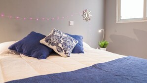 A neatly made bed with blue and white bedding, a decorative wall hanging, and a small potted plant.