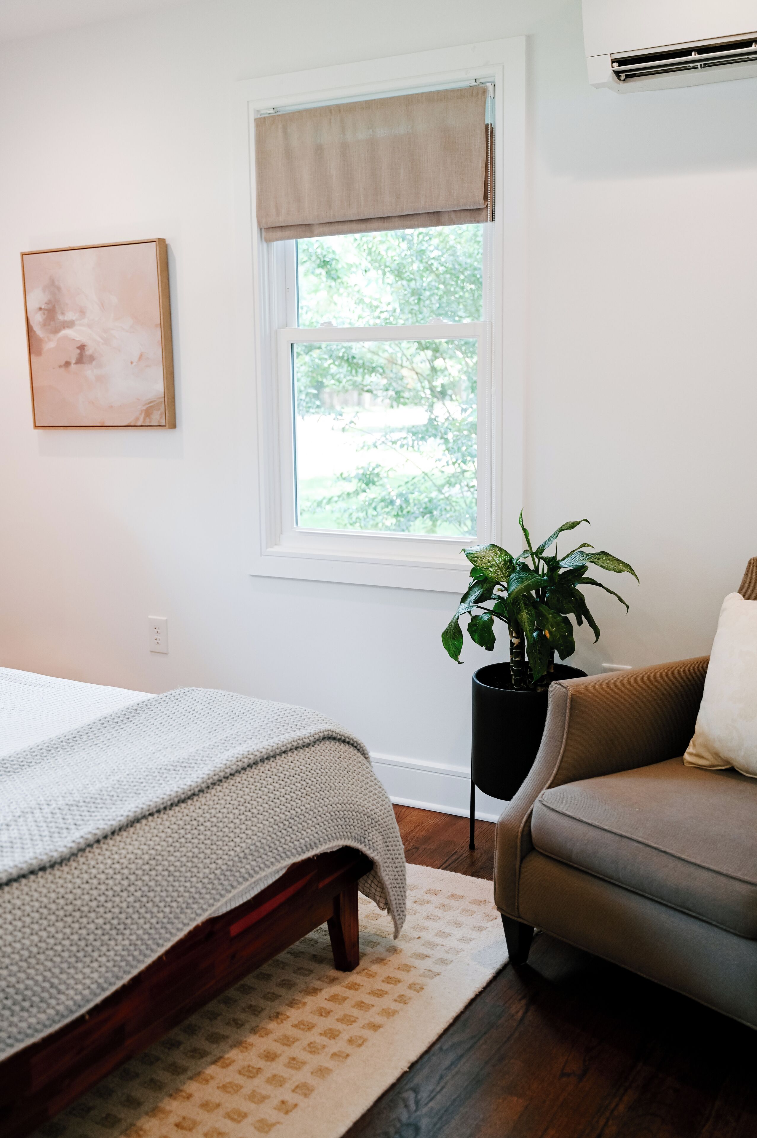 A bedroom with a bed, a window with a view of greenery, a potted plant, and a chair.