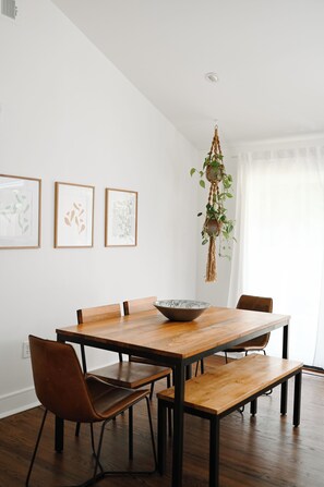 Un comedor con una mesa de madera, cuatro sillas y una planta de macramé colgante.