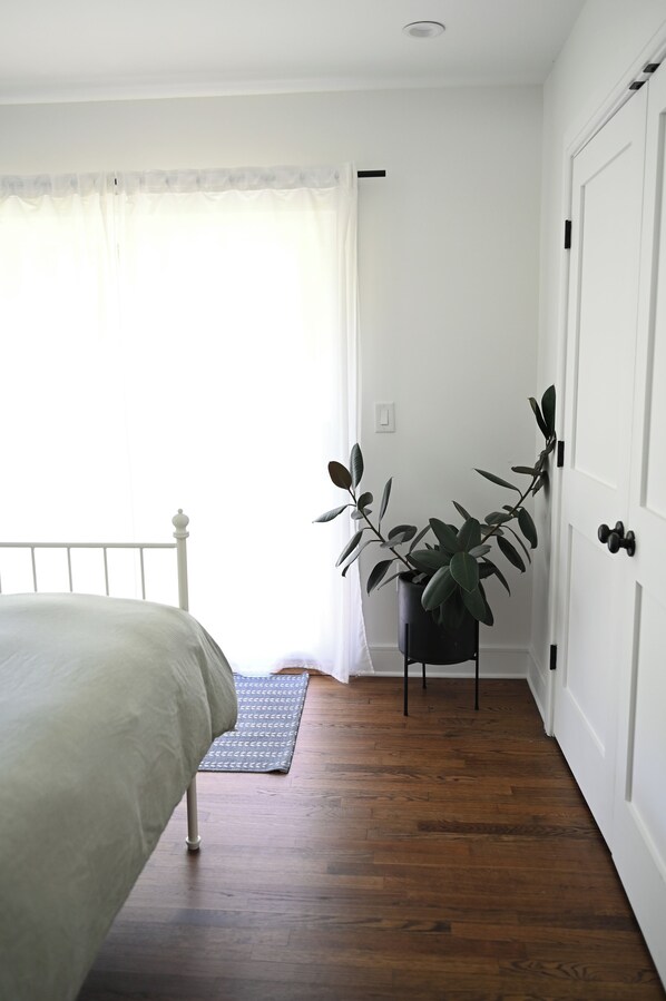 Une chambre à coucher avec un lit, une plante en pot, une porte et une fenêtre avec des rideaux.