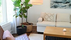 A living room with a sofa, a coffee table, a chair, a floor lamp, and a potted plant. - Charming 2-bedroom house in beautiful Charleston with full kitchen, AC, patio (Charleston)