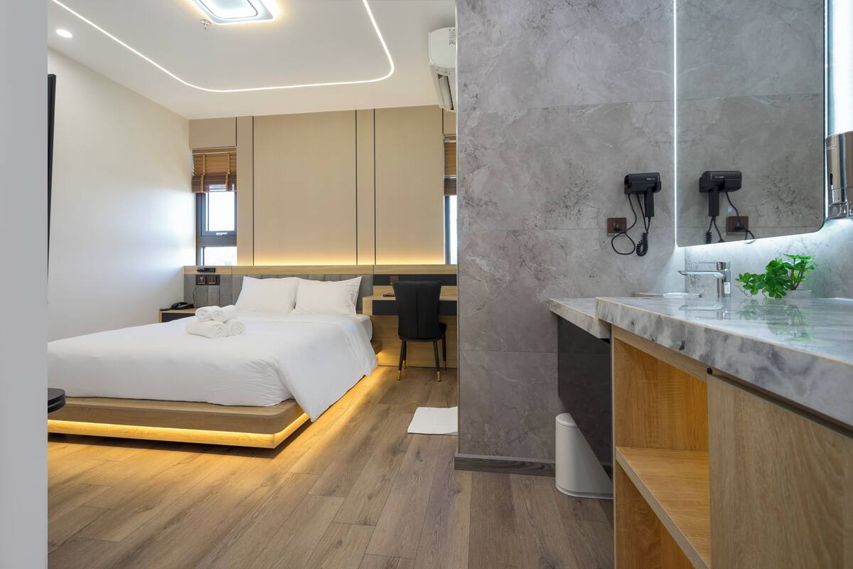Ett modernt hotellrum med en säng, ett skrivbord och ett badrum med en stor spegel.