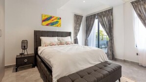 A modern bedroom with a large bed, a bench, a nightstand, and a colorful abstract painting.