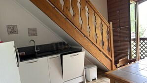 A kitchen with white cabinets, a black countertop, and a wooden staircase. There are two signs on the wall, a sink, and a small trash bin.